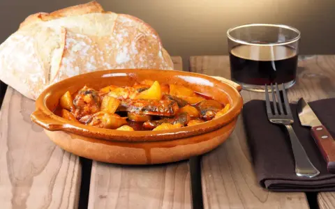 Un plato de all i pebre, con pan rústico y vino tinto, listo para disfrutar.