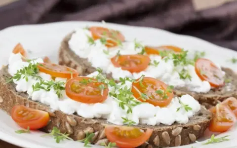Kanapki z ciemnego pieczywa z twarożkiem, pomidorkami koktajlowymi i kiełkami.