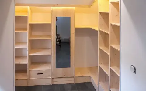 Construction d'une armoire sur mesure avec des portes coulissantes et des étagères en bois clair. Un miroir est intégré.