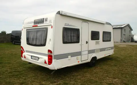 Biała przyczepa kempingowa Caravelair 495 RE na trawie, z widocznym logo MANCZAK.PL.