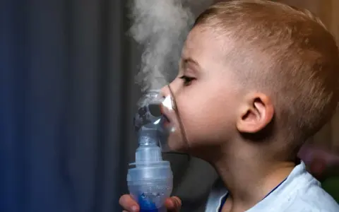 Chłopiec z maską inhalacyjną na twarzy, wdycha parę. Skuteczna inhalacja na katar u dziecka.
