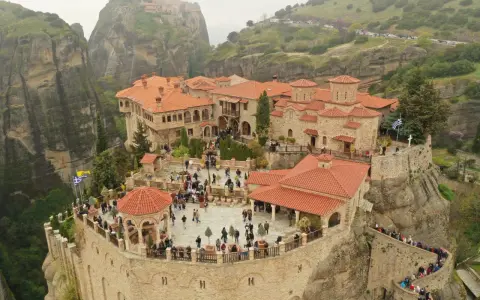 A stunning view of the monasteries of Meteora, perched atop towering rock formations. Visitors explore the courtyards and pathways, a testament to the enduring spirit of this sacred place.