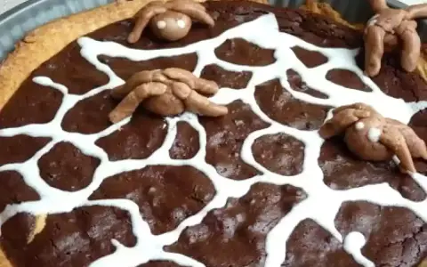 Tarte au chocolat d'Halloween décorée d'une toile d'araignée en glaçage blanc et d'araignées en pâte d'amande.