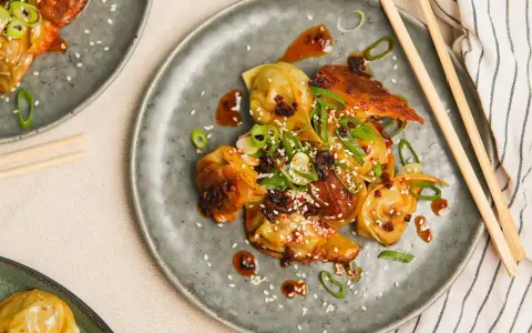 Stekta dumplings med en kryddig sås, toppade med sesamfrön och salladslök. En utsökt dumplings sås som gör rätten komplett.