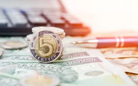 Złota moneta 5 złotych na stosie monet i banknotów. Obok długopis i kalkulator, sugerujące planowanie finansowe i możliwość recoverso rmc.