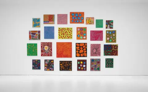 A vibrant collection of paintings by top visual artists, featuring bold colors and abstract patterns, adorns a white gallery wall.