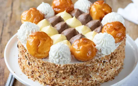 Una deliziosa torta Saint Honoré, con bignè caramellati, panna montata e crema al cioccolato e vaniglia, il tutto ricoperto di granella di nocciole.