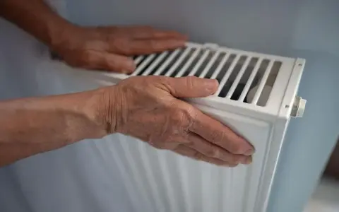 Manos sobre un radiador blanco, sintiendo el calor. El radiador hace ruido, quizás por el agua circulando.
