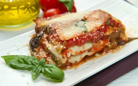 Una fetta di parmigiana di mare pugliese, con melanzane, pomodoro e mozzarella filante, guarnita con basilico fresco.