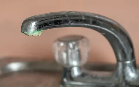 Robinet chromé avec un dépôt de calcaire vert de gris à son extrémité.