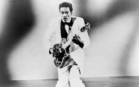 Chuck Berry in weißem Anzug spielt Gitarre, bereit für "Johnny B. Goode".