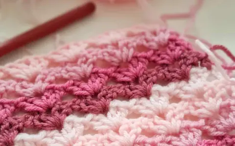 Tejido a crochet con hilo rosa y blanco. Un patrón de chaleco fácil en progreso, con un ganchillo rojo al fondo.
