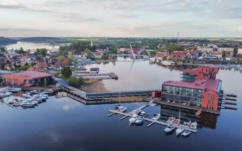 Nowoczesna marina i hotel nad jeziorem, idealne miejsce, by zobaczyć, co zwiedzać na Mazurach. Widać tu wiele łodzi i urokliwe miasteczko.