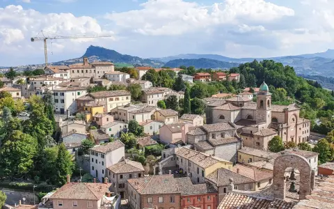 Un borgo pittoresco sulle colline riminesi, con tetti rossi, una chiesa con campanile e un paesaggio verdeggiante sullo sfondo.
