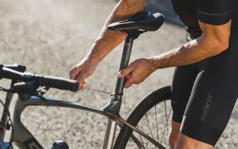 Rowerzysta reguluje wysokość siodełka w rowerze szosowym, używając klucza imbusowego.