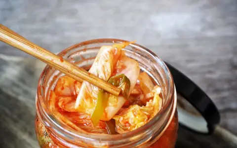Pałeczki bambusowe wyciągają kawałek kimchi z słoika.
