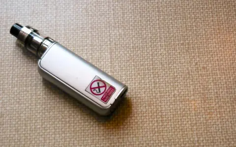 Un vape plateado con una pegatina que dice "I MISS FAGS VAPE SUCKS" y un símbolo de prohibido.