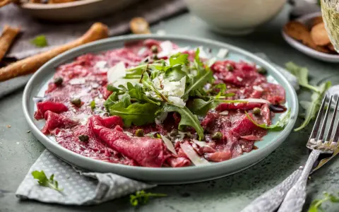 En tallrik med tunt skivad råbiff, toppad med ruccola, parmesan och kapris. Perfekt vin till carpaccio.