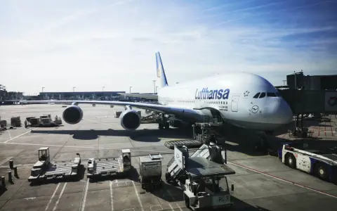 Lufthansa A380 na płycie lotniska we Frankfurcie. W tle widać inne samoloty i budynki terminali, typowe dla lotnisk w Niemczech.