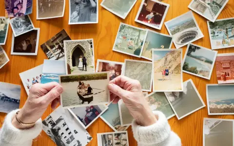 Mani anziane sfogliano vecchie foto stampate su un tavolo di legno, un modo per conservare le foto stampate e i ricordi.
