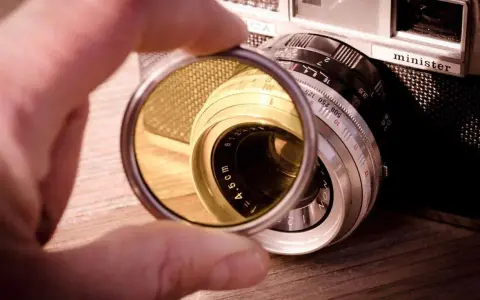 Une main tient un filtre protection objectif devant un vieil appareil photo argentique.