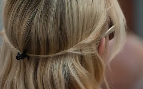 Piaskowy blond włosów spięty warkoczem z tyłu głowy. Delikatne pasma opadają na ramiona.