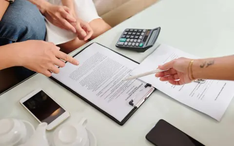 Des mains examinent un contrat de bail verbal, avec un téléphone, une calculatrice et une théière à proximité.