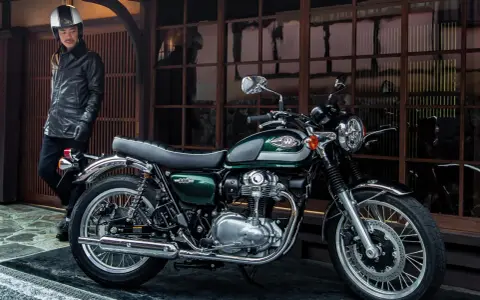 Mężczyzna w skórzanej kurtce i kasku stoi obok klasycznego motocykla Kawasaki W800 w kolorze ciemnozielonym.
