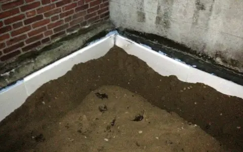Styrodurplatten werden auf Bitumen geklebt, um eine Dämmung zu schaffen. Sand liegt auf den Platten.