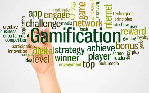 Ręka pisze słowo "Gamification" otoczone chmurą powiązanych terminów, takich jak "gra", "nagroda", "bonus", "strategia", "motywacja" i "sieć". Grywalizacja w akcji!