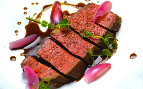 Une succulente entrecôte de bœuf, tranchée et nappée d'une sauce riche, accompagnée de jeunes pousses et d'oignons rouges marinés.