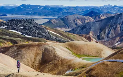 Un randonneur solitaire explore les paysages colorés et volcaniques de Landmannalaugar, un trek inoubliable en Islande.