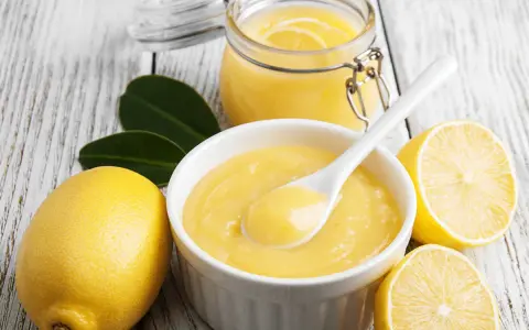 Aksamitny curd cytrynowy w miseczce, obok cytryny i słoiczek z tym pysznym kremem. Idealny do deserów!