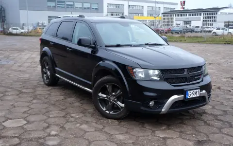 Czarny Dodge Journey 3.6 zaparkowany na placu z kostki brukowej. W tle budynki i inne samochody.