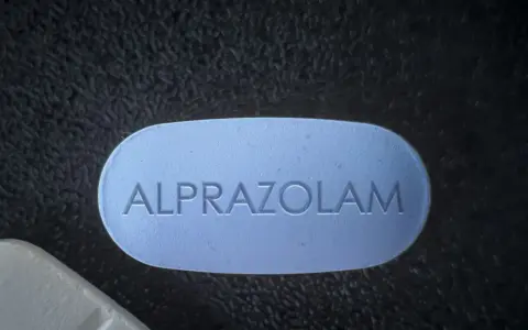 Niebieska tabletka z napisem "ALPRAZOLAM" leży obok białej. Uważaj na niebezpieczne skutki połączenia xanax i alkohol.