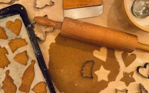 Pepparkaksdeg recept förbereds med kavel och pepparkaksformar. Färdiga pepparkakor ligger på en plåt.