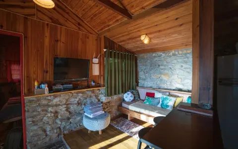 Un salon cosy en bois et pierre, avec canapé, TV et table. Idéal pour savoir comment agrandir une pièce avec style.