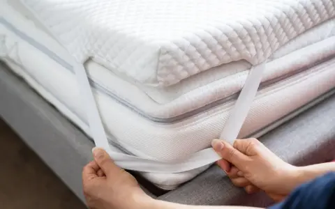 Mains ajustant les élastiques d'un surmatelas blanc et moelleux. Un surmatelas améliore le confort et la protection de votre matelas.