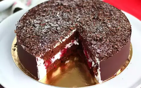 Tarta Selva Negra, con capas de bizcocho de chocolate, nata montada y cerezas, cubierta de virutas de chocolate y un toque de azúcar glas.