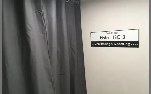 Grauer Schallschutzvorhang im Test. Ein Schild mit "Produkt-Test Hofa - ISO 3" und "www.hellhoerige-wohnung.com" hängt an der Wand.