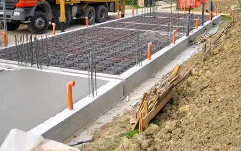 Costruzione in corso: rete di armatura e tubi arancioni per l'aerazione vespaio. Cemento fresco e un camion Beton.