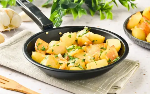 Patatas al ajillo recién hechas en sartén, con perejil fresco y ajos picados. ¡Un plato sencillo y delicioso!