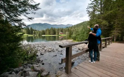 Coppia ammira il lago dei caprioli, con montagne sullo sfondo e una casa tra gli alberi.