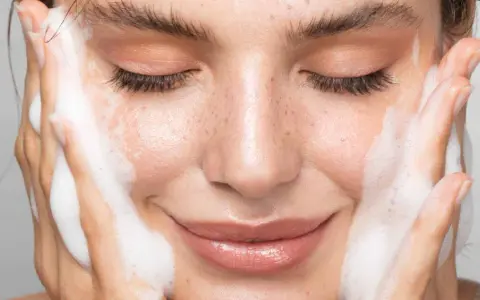 Une femme au visage frais, les yeux fermés, savoure la mousse d'un nettoyant. La définition de la pureté.