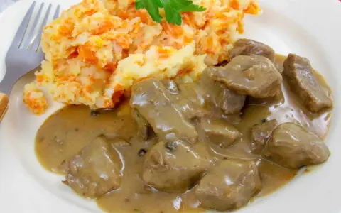 Un plat de rognon de boeuf en sauce, servi avec une purée de pommes de terre et carottes, garni de persil.