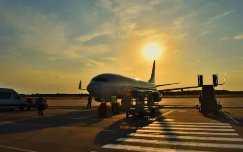 Samolot flydubai na lotnisku o zachodzie słońca. Pracownicy przygotowują bagaż rejestrowany, sprawdzając jego wymiary przed załadunkiem.