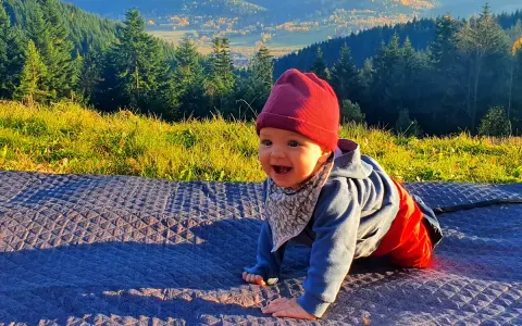 Uśmiechnięte dziecko na kocyku, w tle góry i las. Jakby czytało psalm 131 tekst o spokoju.