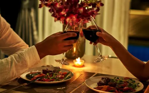 Para romantyczna kolacja: para wznosi toast winem przy świecach, z pięknymi kwiatami i pysznym jedzeniem.