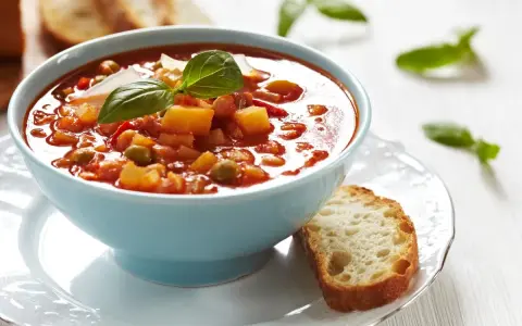 Aksamitna zupa solferino w błękitnej miseczce, ozdobiona bazylią i parmezanem, podana z chrupiącą grzanką.