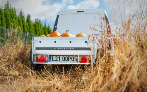 Biała furgonetka z przyczepą pełną dyni, gotowa do transportu. Spedytor czeka na załadunek.